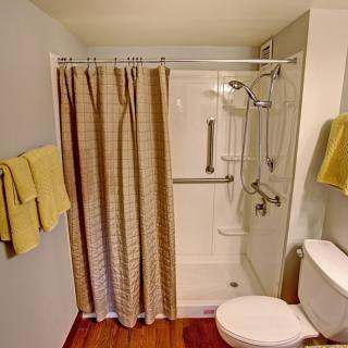 A bathroom with a shower area equipped with handrails, a curtain, and a toilet with yellow towels.