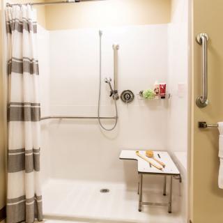A modern, accessible bathroom shower equipped with a shower chair and grab bars.