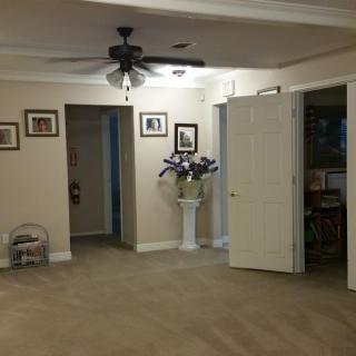 A spacious living room with a ceiling fan, decorated walls, and an open door leading to another room.