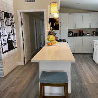 A modern kitchen featuring a central island with a fruit bowl, white cabinets, and pendant lighting.
