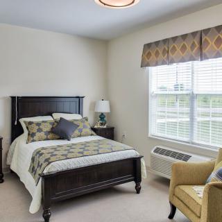 A cozy bedroom with a bed, armchair, and window providing natural light.