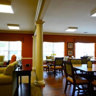 A cozy dining area with tables and chairs, featuring decorative columns and bright windows.