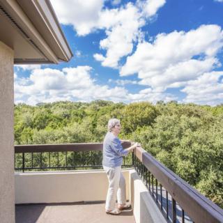 A person enjoying the view from a balcony overlooking a lush green landscape under a partly cloudy sky.