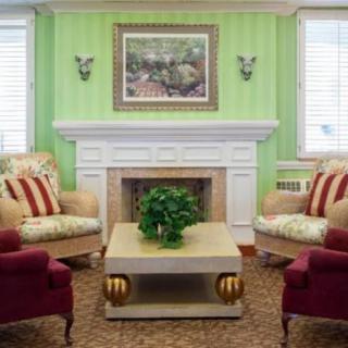 A cozy living room with green walls, featuring a white fireplace, comfortable armchairs, and a central coffee table adorned with a plant.