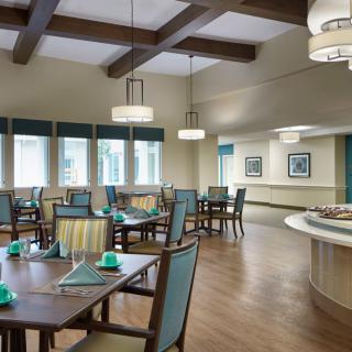 A well-lit dining room with neatly arranged tables and chairs, featuring elegant lighting and wooden flooring.