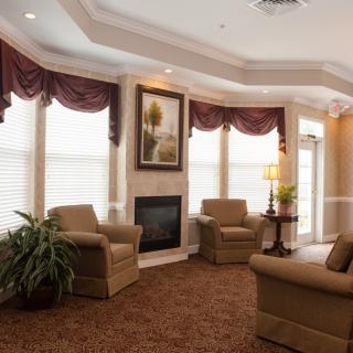 A cozy living room with armchairs arranged around a fireplace, featuring elegant window treatments and warm lighting.