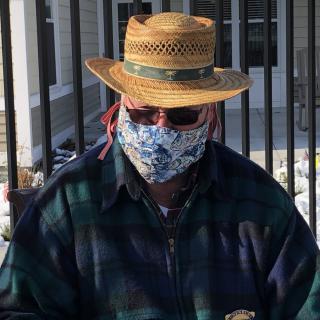 A person wearing a straw hat, sunglasses, and a floral face mask outdoors.