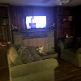 A cozy living room with a television mounted above a fireplace, surrounded by couches.
