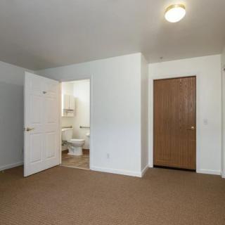 An empty bedroom with a beige carpet and adjoining bathroom.