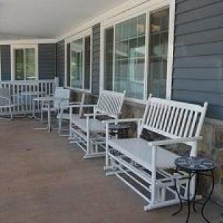 A row of white rocking chairs on a porch with large windows.