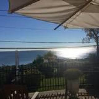 A picturesque patio with an ocean view at sunset, shaded by a large umbrella.