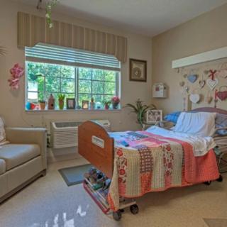 A cozy hospital room with a quilt-covered bed and decorative items by the window.