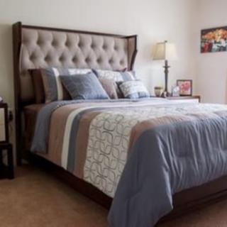 A cozy bedroom with a neatly made bed, featuring a tufted headboard and soft pillows.