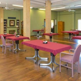A spacious dining area with red tablecloth-covered tables and chairs, featuring a mirrored wall and wooden flooring.