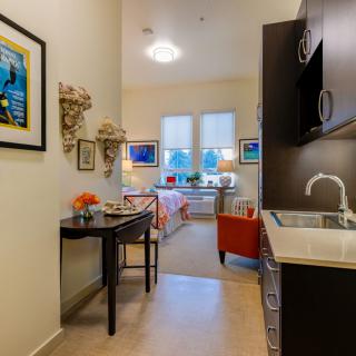 A cozy interior featuring a kitchenette leading to a brightly lit living area, adorned with artwork and stylish furniture.