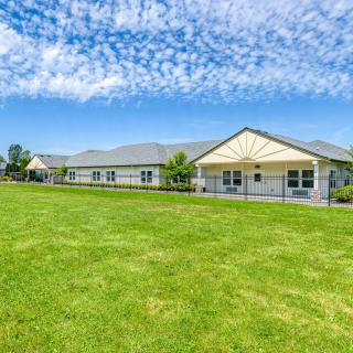 A single-story building with a large green lawn under a blue sky with clouds.