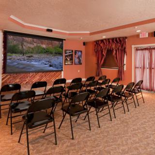 A small indoor movie theater with rows of folding chairs facing a large screen.