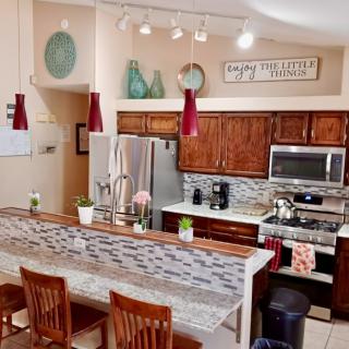 A modern kitchen with stainless steel appliances, wooden cabinets, and a center island adorned with decorative vases and red pendant lights.