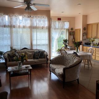 A cozy living room and kitchen area with an open floor plan, featuring wooden flooring and sunlight streaming through large windows.