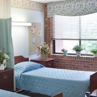 A hospital room with two beds and a window displaying potted plants.