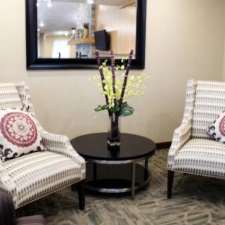A cozy seating area featuring two patterned chairs, a round table with floral arrangement, and a large wall mirror.