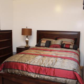 A cozy bedroom with a neatly made bed, wooden furniture, and a lamp.