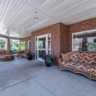 A cozy outdoor porch with cushioned seating and potted plants against a brick wall backdrop.
