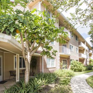 A tranquil view of a residential apartment building surrounded by lush greenery and a winding pathway.