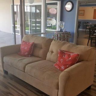 A cozy living room featuring a beige sofa with red patterned cushions, set against a backdrop of large windows and hardwood floors.