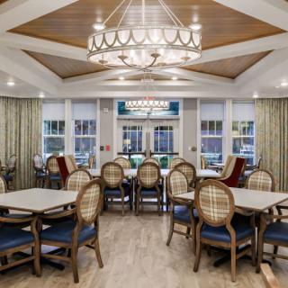 A well-furnished dining area with multiple tables and chairs, featuring a central chandelier and wooden ceiling accents.