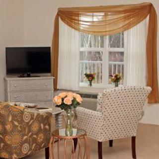 Cozy living room with patterned chairs, a TV, and elegant window drapes.