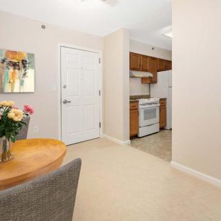A cozy apartment interior featuring a small kitchen and dining area with a round table, chairs, and flowers on the table.