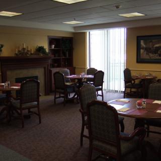 A cozy dining room with several tables and chairs, a fireplace, and large windows.