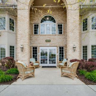 Elegant building entrance with wicker chairs and landscaped surroundings.