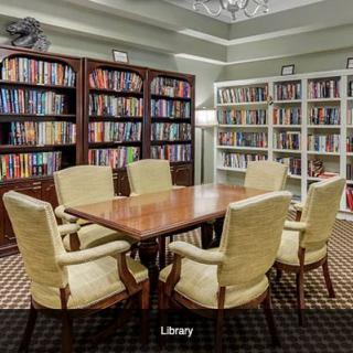 A cozy library with bookshelves and a reading table surrounded by chairs.
