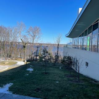 A serene view featuring a building beside a body of water, framed by trees and a clear blue sky.