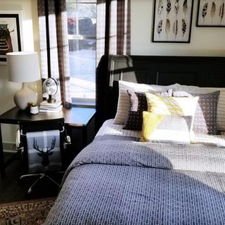 A cozy and well-decorated bedroom with a neatly made bed, a side table with a lamp, and framed artwork on the walls.
