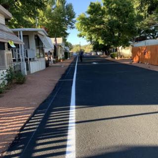 A quiet residential street lined with trees and houses, freshly paved with a white line down the center.