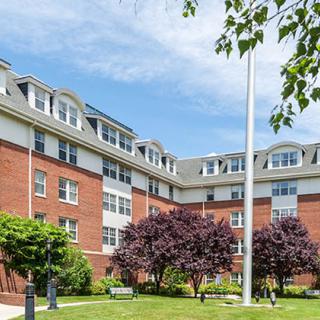 A multi-story brick residential building with a flagpole and trees in front.