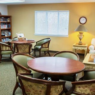 A cozy living room with round tables, chairs, bookshelves, and a lamp.