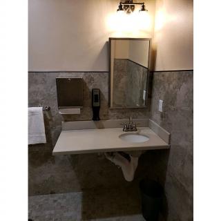 A bathroom with a sink, mirror, tile walls, and a mounted soap dispenser.