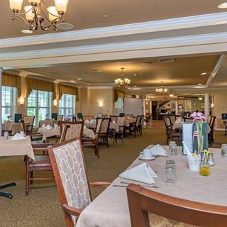 An elegant dining room with neatly arranged tables and chairs, well-lit by chandeliers.