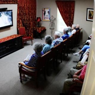 A group of seniors sitting in a living room watching television together.