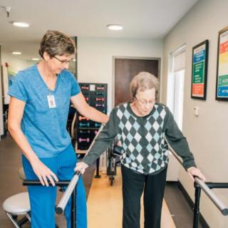 A healthcare professional assists an elderly person during a physical therapy session.