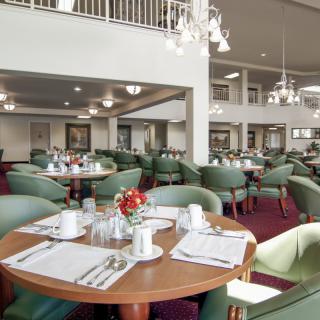 A spacious restaurant dining area with neatly arranged tables and chairs, illuminated by elegant chandeliers.