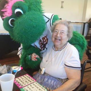 A cheerful elderly woman enjoys a bingo game with a friendly mascot.