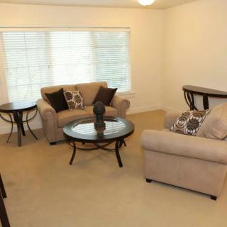 A cozy living room with beige sofas, a round glass coffee table, and decorative cushions.