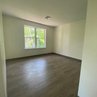 A bright, empty room with a large window and wooden flooring.