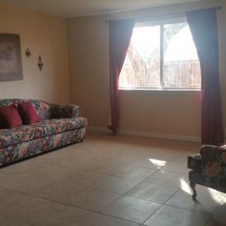 A cozy living room with a floral sofa and armchair, featuring a large window with curtains.