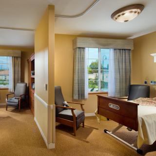 A well-lit hospital room with a bed, chairs, and large windows.